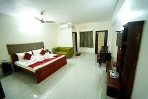 A hotel room with a bed, a green armchair, a TV, and a wooden cabinet.