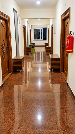 A hallway with polished tile flooring, wooden doors, and a fire extinguisher mounted on the wall. - Hotel Kvr Residency Tada  (Tada)