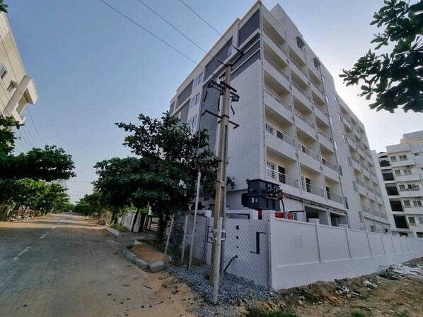 Un immeuble résidentiel à plusieurs étages, doté de balcons, d’une entrée sécurisée et donnant sur une rue en arrière-plan.