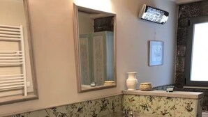 A bathroom with a large vessel sink, a mirror, a wall-mounted heater, and a stone accent wall.