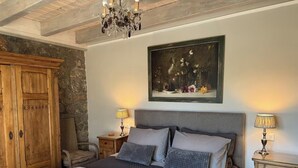 A bedroom with a large bed, a wooden wardrobe, a painting, and a chandelier.