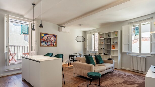 A modern living room with a sofa, chairs, a coffee table, and a kitchen area with a fridge and shelves.