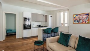 A modern kitchen with white cabinets, a dining area with a bar stool, a sofa with green cushions, and a painting on the wall.