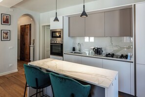 A modern kitchen with a marble countertop, two bar stools, a built-in oven, and pendant lighting. - Casa Momo - Modern stay in the heart of Lucca (Lucca)