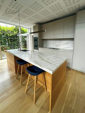 Una cocina moderna con encimera de mármol, taburetes de madera y electrodomésticos integrados.