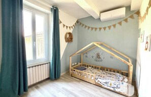 Ein Kinderzimmer mit einem hölzernen Etagenbett, einem Fenster mit Vorhängen, einem Heizkörper und einer Wand-Klimaanlage.