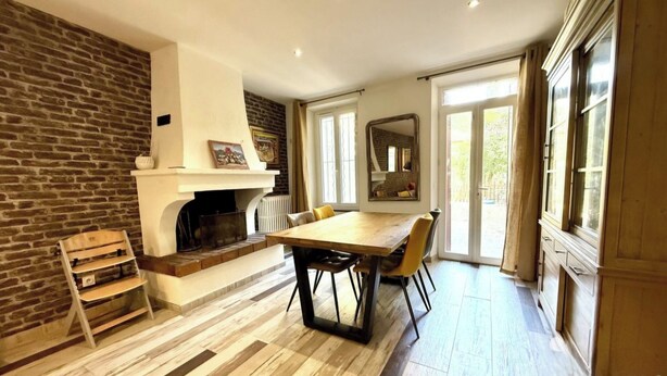A dining area with a fireplace, a wooden bench, a table with chairs, and a view through a glass door. - Large family home in the heart of the village (Sainte-Cécile-les-Vignes)