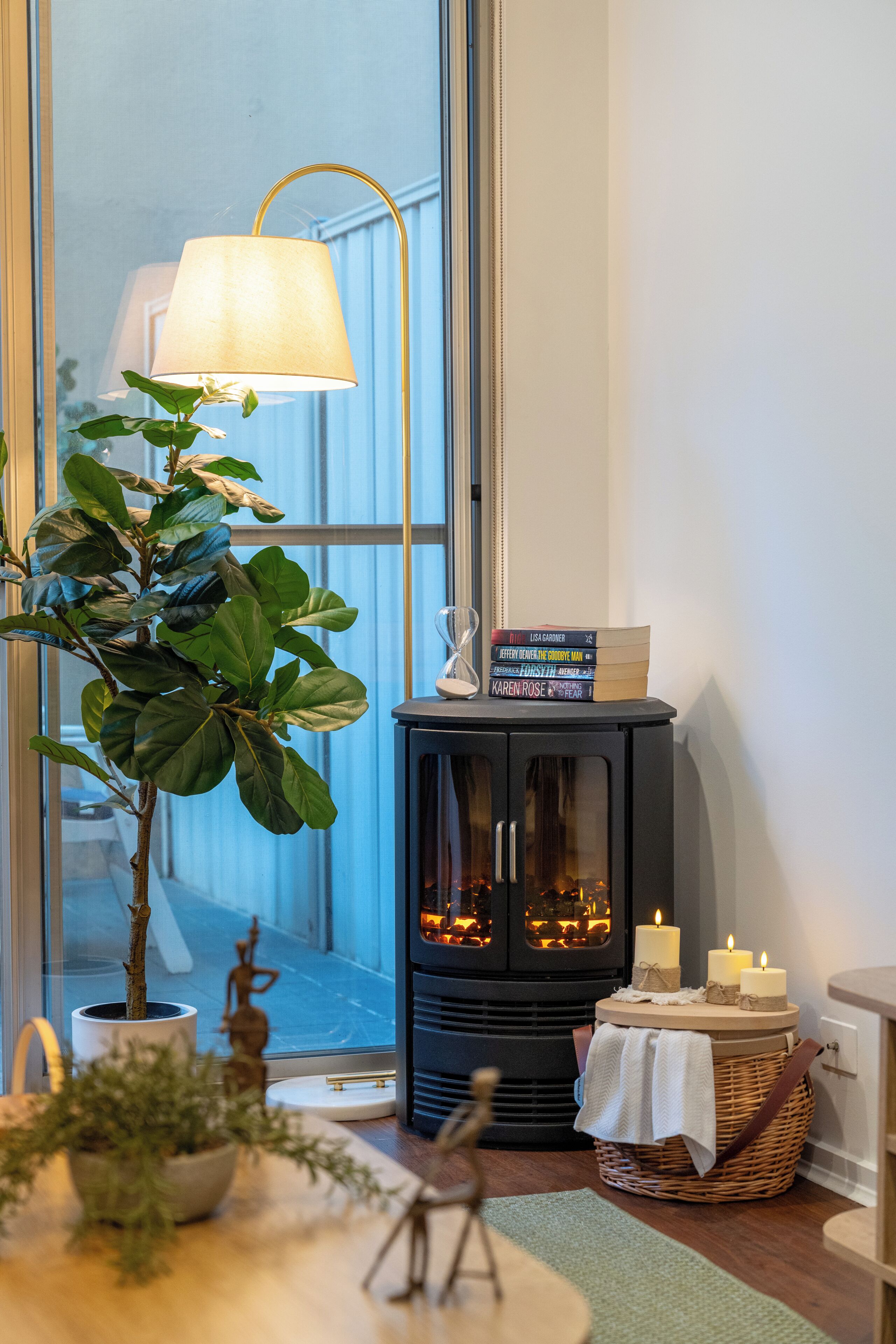Et hyggeligt rum med et stort vindue, en gulvlampe, en reol med bøger, en pejs og en potteplante.