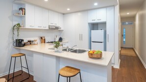 Eine moderne Küche mit weißen Schränken, einer zentralen Kochinsel inklusive Sitzgelegenheiten, einem Kühlschrank und einer Spüle.