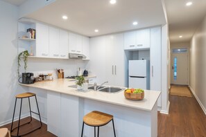Eine moderne Küche mit weißen Schränken, einer zentralen Kochinsel inklusive Sitzgelegenheiten, einem Kühlschrank und einer Spüle.