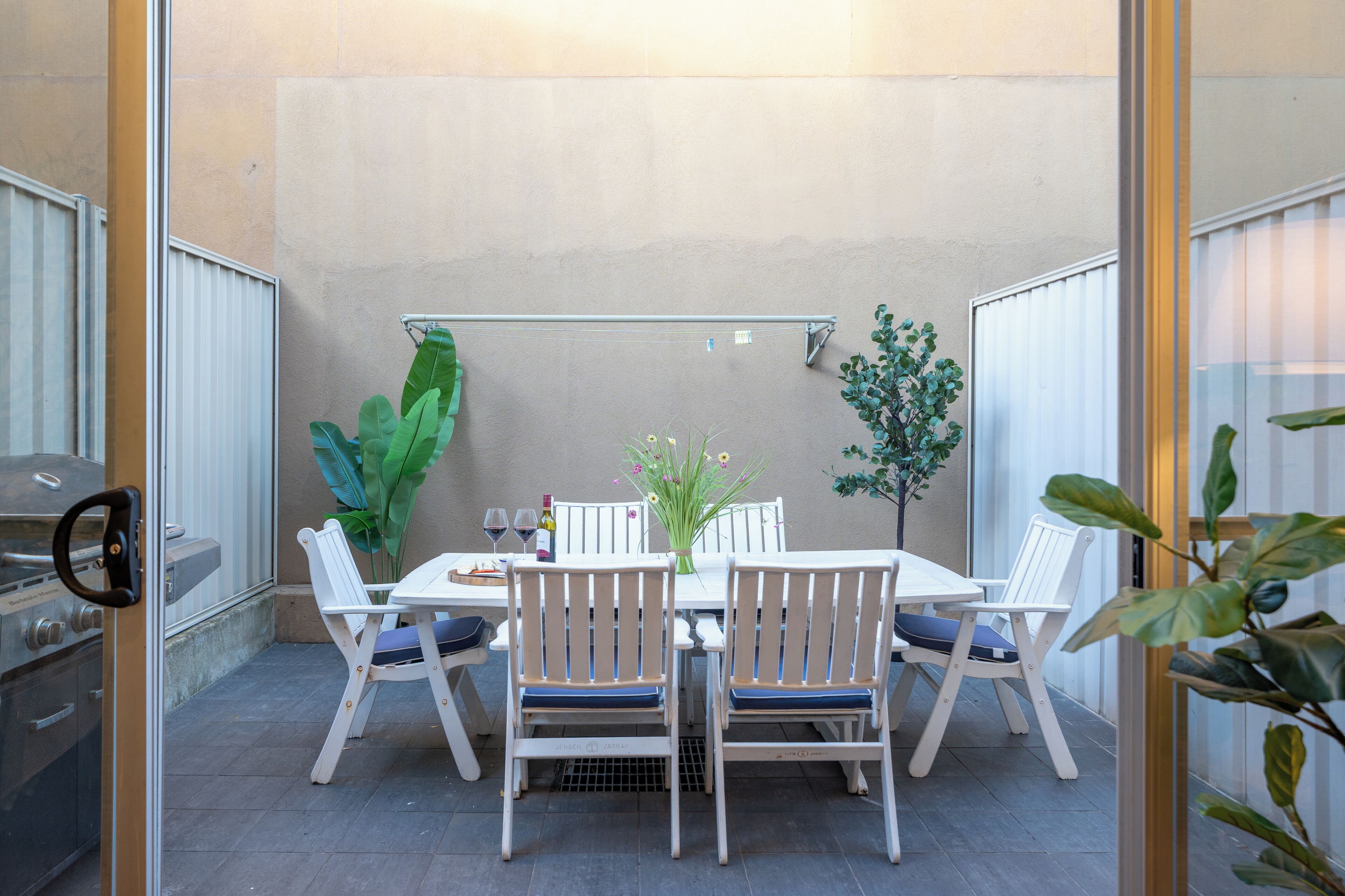 A patio with a table and chairs, a grill, and potted plants.