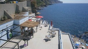 En terrass vid havet med utomhusmöbler, ett räcke och utsikt över havet.