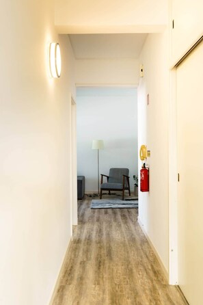 A hallway with a wooden floor, a chair, a lamp, and a fire extinguisher. - Enjoy the city center at fully equipped 2 BR w/ AC (Funchal)