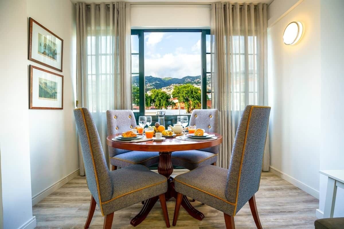 Een eetruimte met een tafel voor twee, een raam met uitzicht op het landschap, en ingelijste foto's aan de muur.