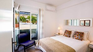 Ett hotellrum med en säng, en stol, ett nattduksbord, en lampa, ett fönster med utsikt och en luftkonditioneringsanläggning.