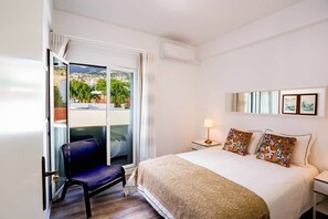 Ein Hotelzimmer mit Bett, Stuhl, Nachttisch, Lampe, Fenster mit Aussicht und Klimaanlage.