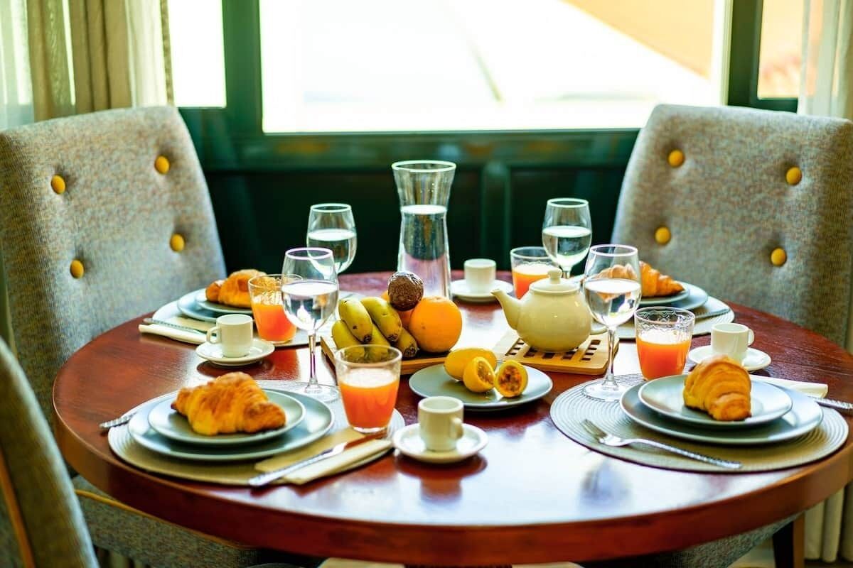 A breakfast table with croissants, fruit, juice, and a teapot.