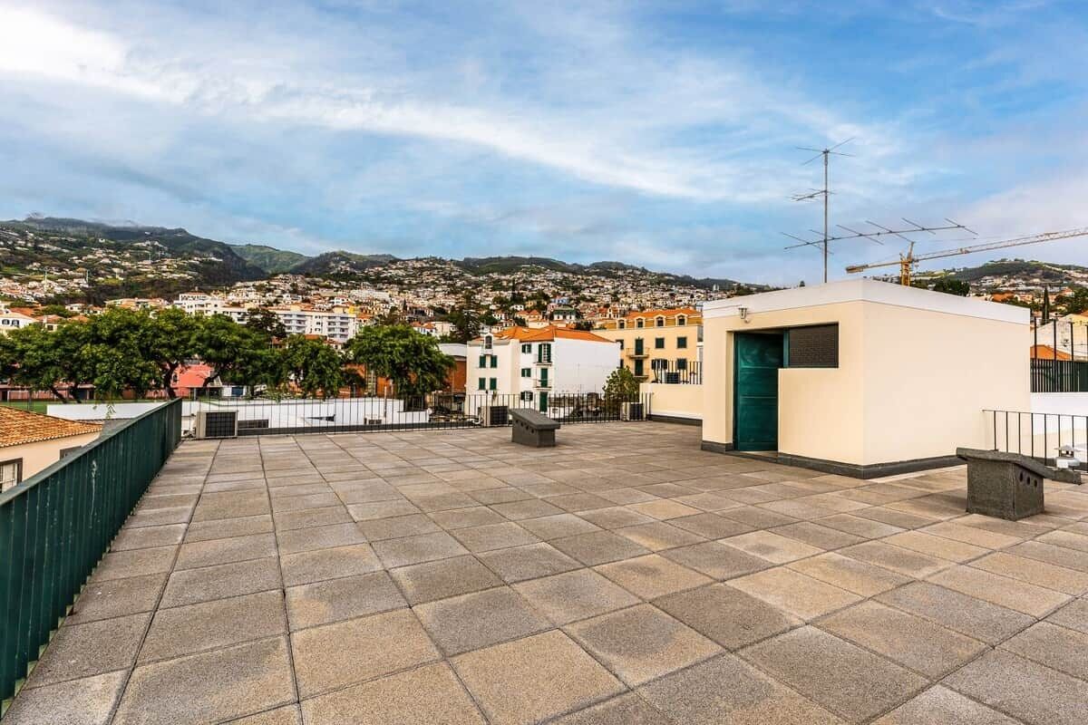 A rooftop terrace with a view of a town, a small building with a green door, and a satellite dish.