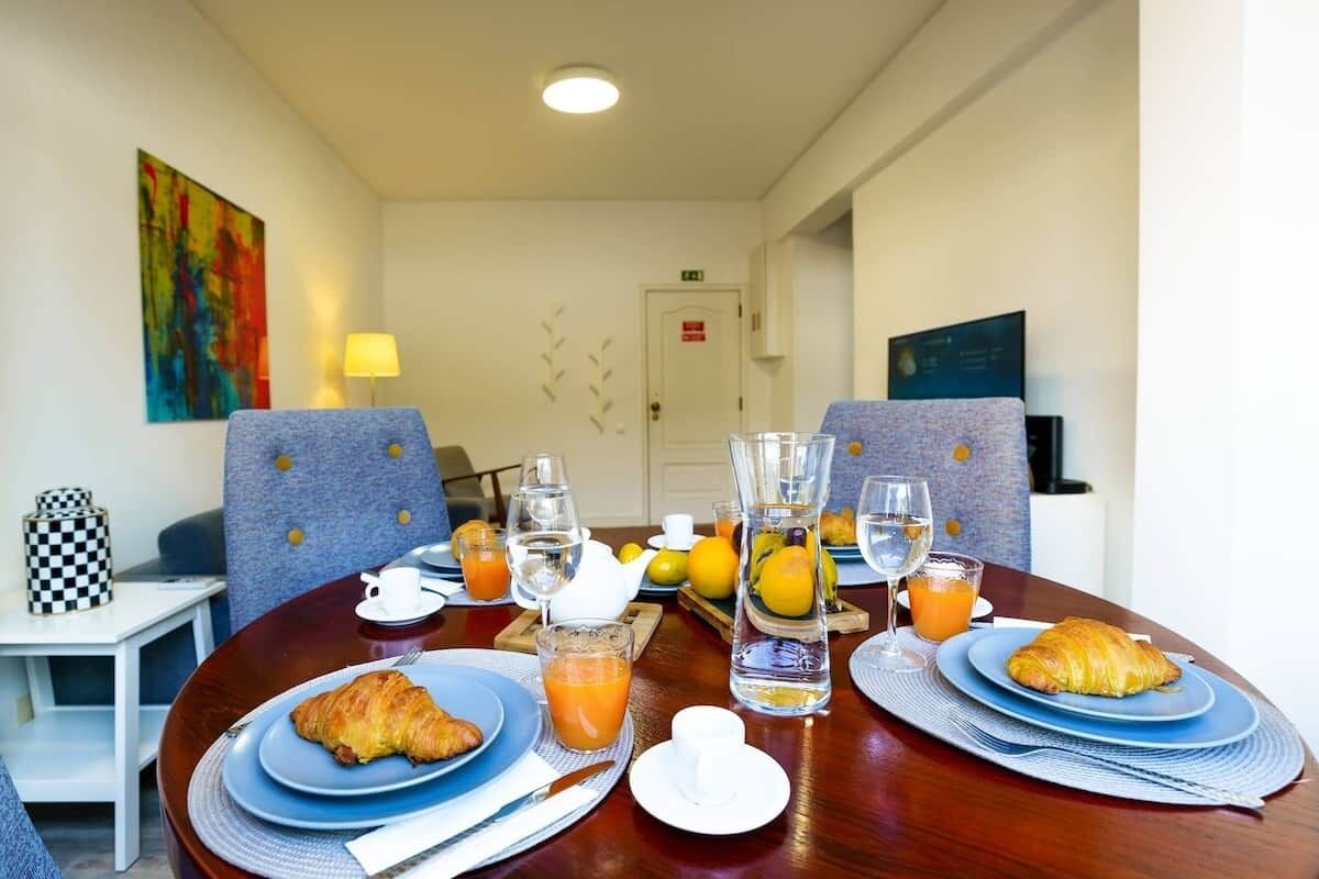 Une table de petit-déjeuner avec des croissants, du jus d’orange et des verres d’eau.