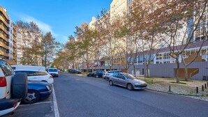 Eine Straße mit parkenden Autos und Bäumen, Gebäude an beiden Seiten und einem klaren Himmel.