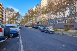 A street lined with parked cars and trees, buildings on both sides, and a clear sky. - Modern apartment with pool and garage (Lisbon)