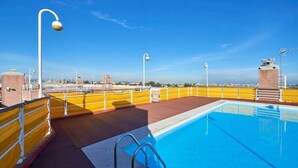 Ein Pool auf dem Dach mit freiem Blick auf die Stadtlandschaft, gelbliche Geländer und einige Straßenlaternen.