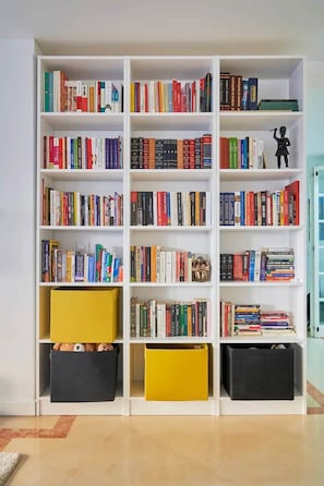 A white bookshelf with multiple shelves filled with books and two yellow storage boxes. - Modern apartment with pool and garage (Lisbon)