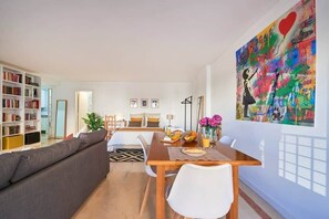 Ein modernes Wohnzimmer mit einer Couch, einem Esstisch mit Stühlen, einem Bücherregal und einem großen abstrakten Gemälde an der Wand.