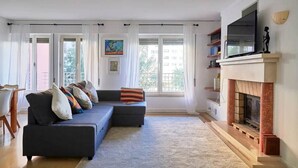 Ein Wohnzimmer mit einer Couch, einem Kamin und großen Fenstern.