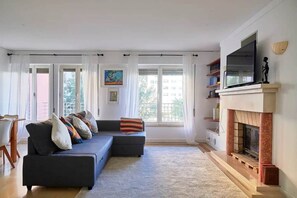 A living room with a sofa, fireplace, and large windows. - Modern apartment with pool and garage (Lisbon)