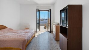 A bedroom with a bed, a dresser, a wardrobe, and a sliding glass door leading to a balcony.
