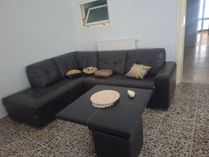 Un salon avec un canapé en cuir foncé, une petite table basse agrémentée d’objets décoratifs, un tapis à motifs et une fenêtre à cadre blanc.