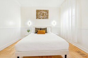 Een slaapkamer met een groot bed, witte muren, een houten vloer en een schilderij aan de wand.