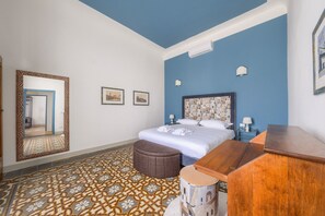 Ein Hotelzimmer mit einem Bett, einem Holzschrank, einem runden Hocker, einem gemusterten Boden, einem großen Spiegel und zwei Wandlampen.