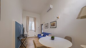 Huoneessa on pyöreä ruokapöytä, sohva, televisio ja ikkuna, jossa on verhot.