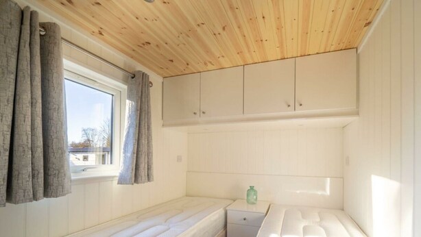 Een kamer met een houten plafond, een raam met gordijnen, een bed, een klein tafeltje en een kast.