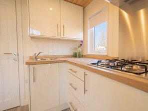 Eine Küche mit weißen Schränken, einer Holzausziehtheke, einem Gasherd und einem Fenster.