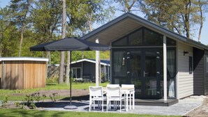 Een modern huis met een overdekte patio, een eethoek met stoelen en een groot raam.
