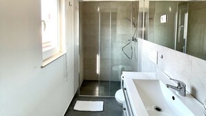 Et moderne badeværelse med et glasafskærmet brusebad, et stort spejl og en hvid vask.