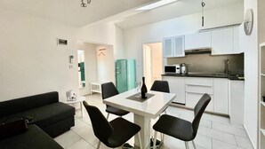 En kompakt opholdsstue med spisebord, sorte stole, en sort sofa, et tekøkken og et lyseblåt køleskab.