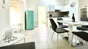 Et moderne køkken med et grønt køleskab, hvide skabe og et spiseområde med et bord og stole.