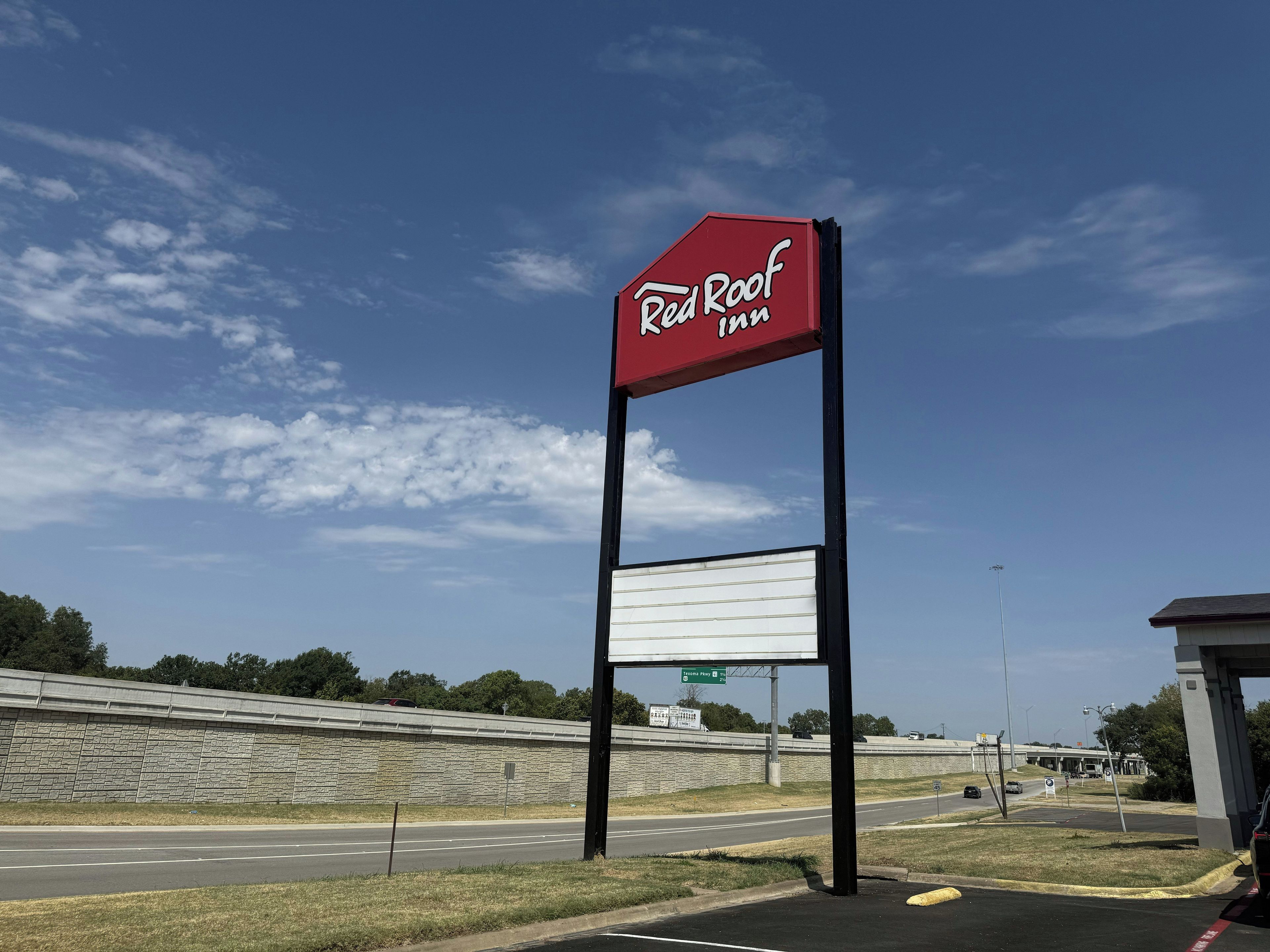 A Red Roof Inn sign with a blank billboard below it, set against a clear sky with a highway in the background.