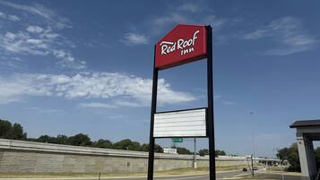 A Red Roof Inn sign with a blank billboard below it, set against a clear sky with a highway in the background.