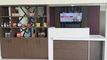 A reception area with a wooden cabinet stocked with snacks and a television displaying a promotional screen.