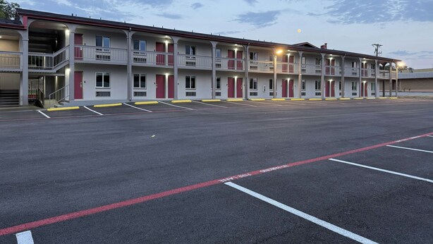 Motel amb diverses plantes, balcons i un aparcament amb places delimitades.