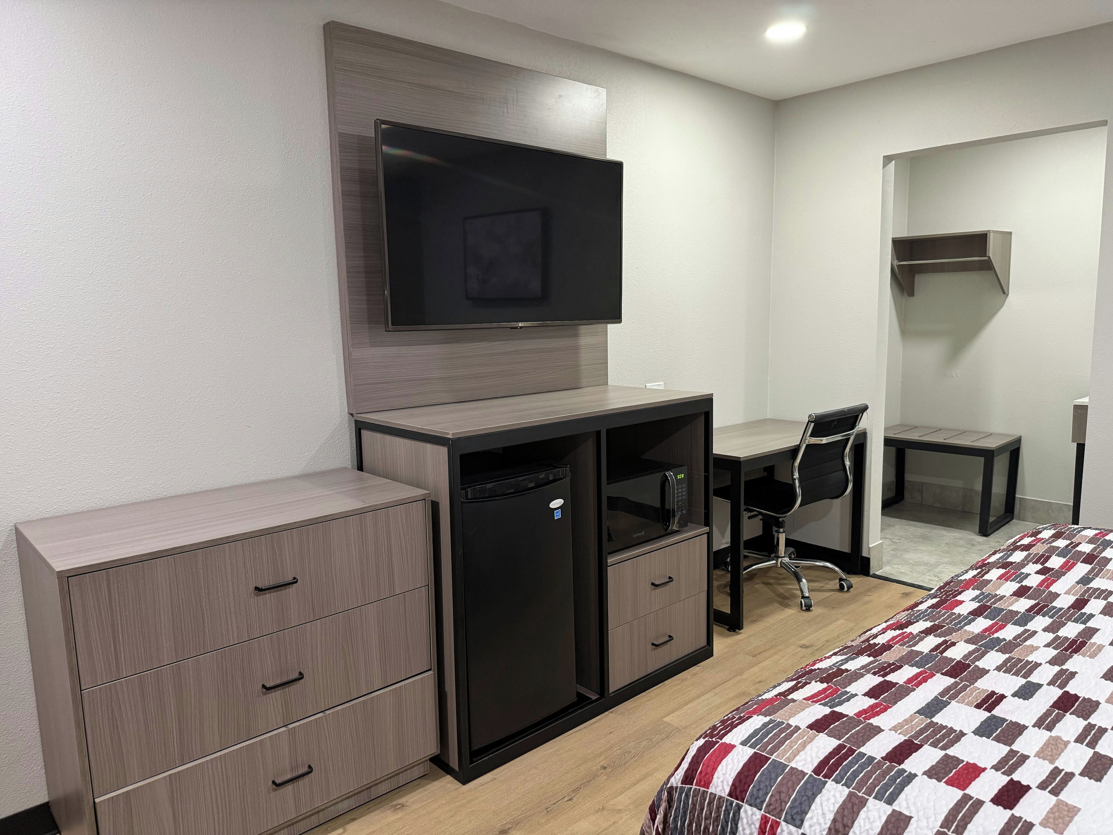 A hotel room with a bed, a desk, a television, a wardrobe, and a microwave.