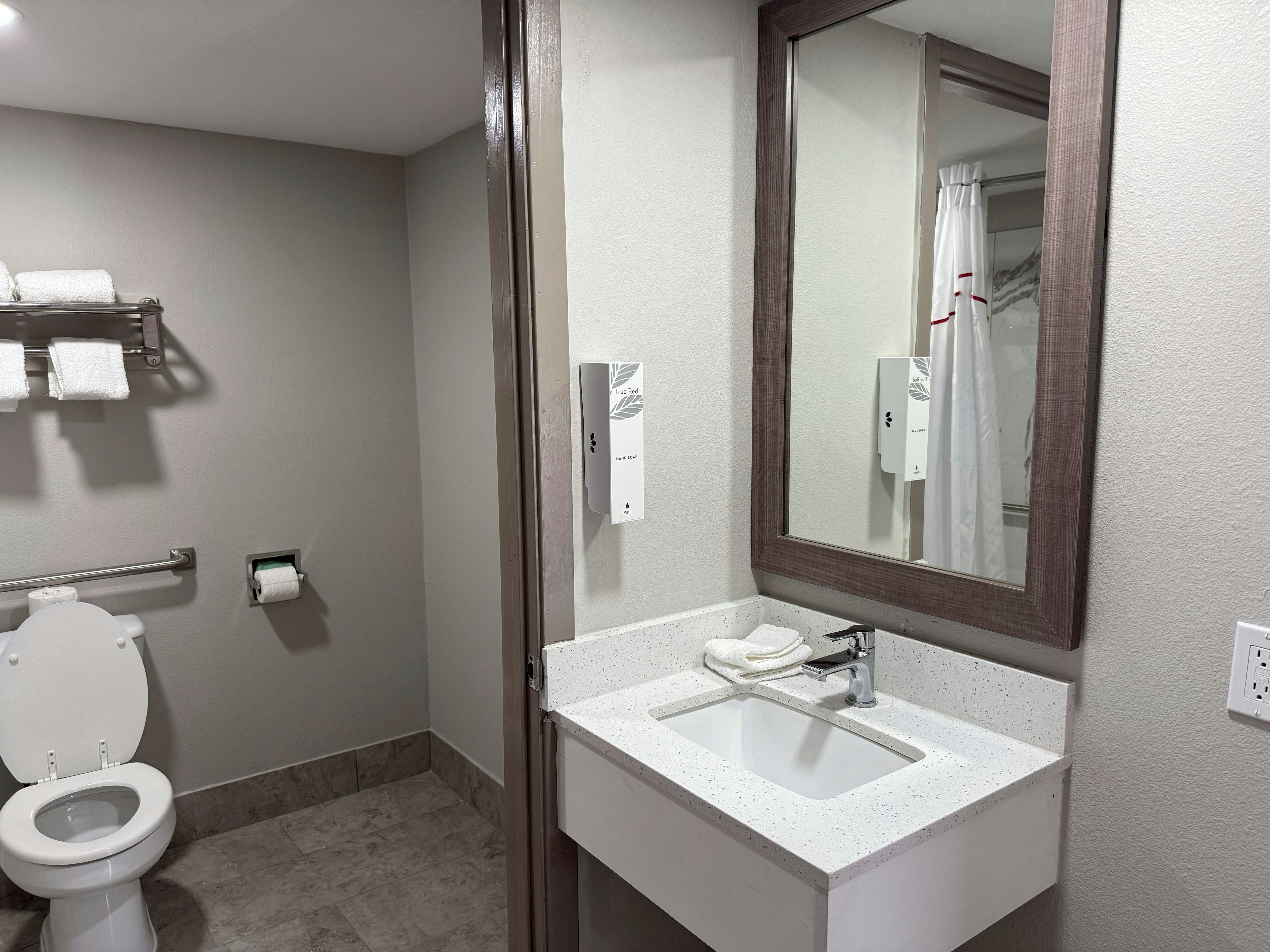 Ein Badezimmer mit Toilette, Waschbecken, Spiegel, Handtuchhalter und Handtrockner.