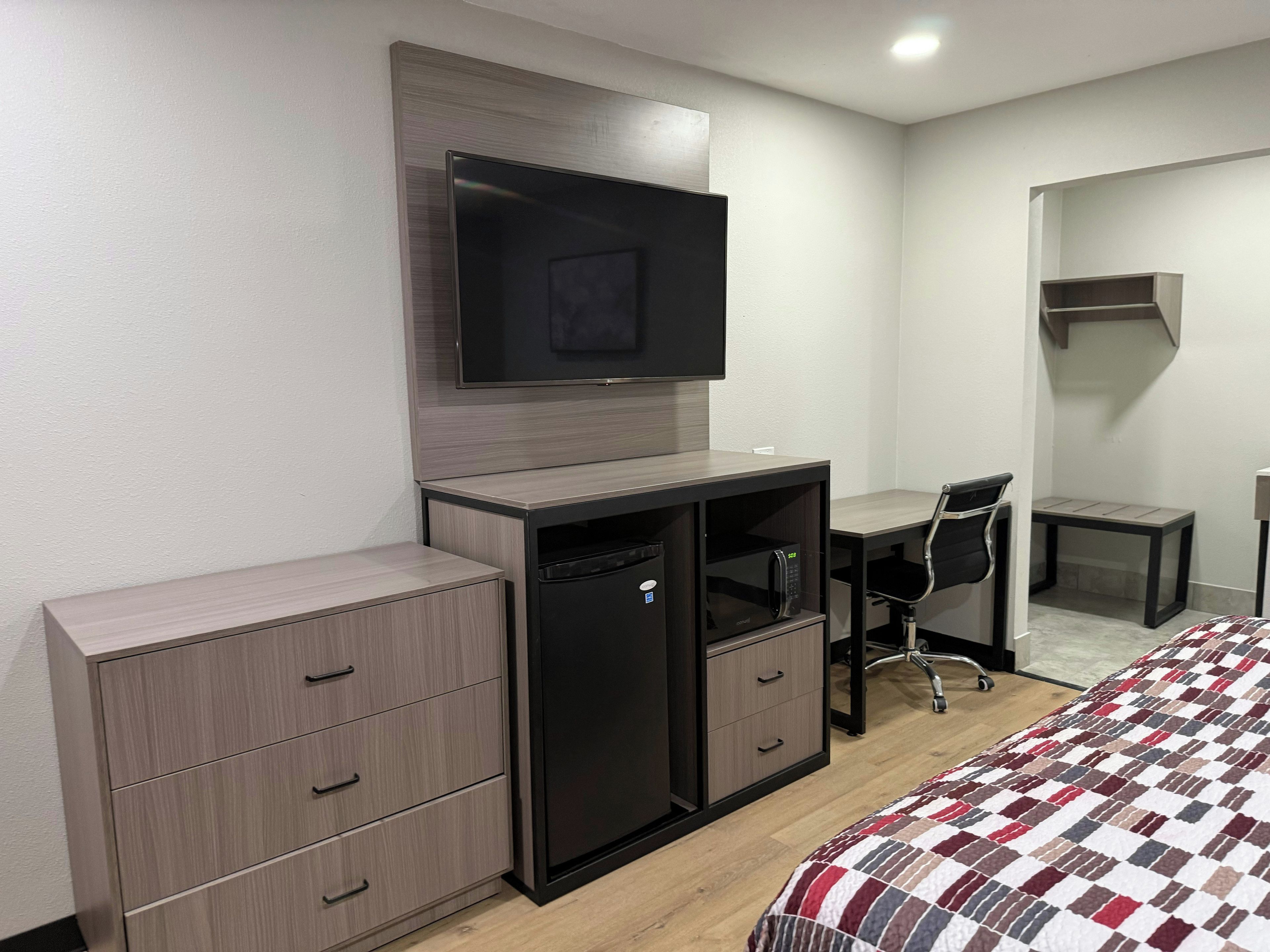 Una habitación de hotel con cama, escritorio, televisor, armario y espejo.