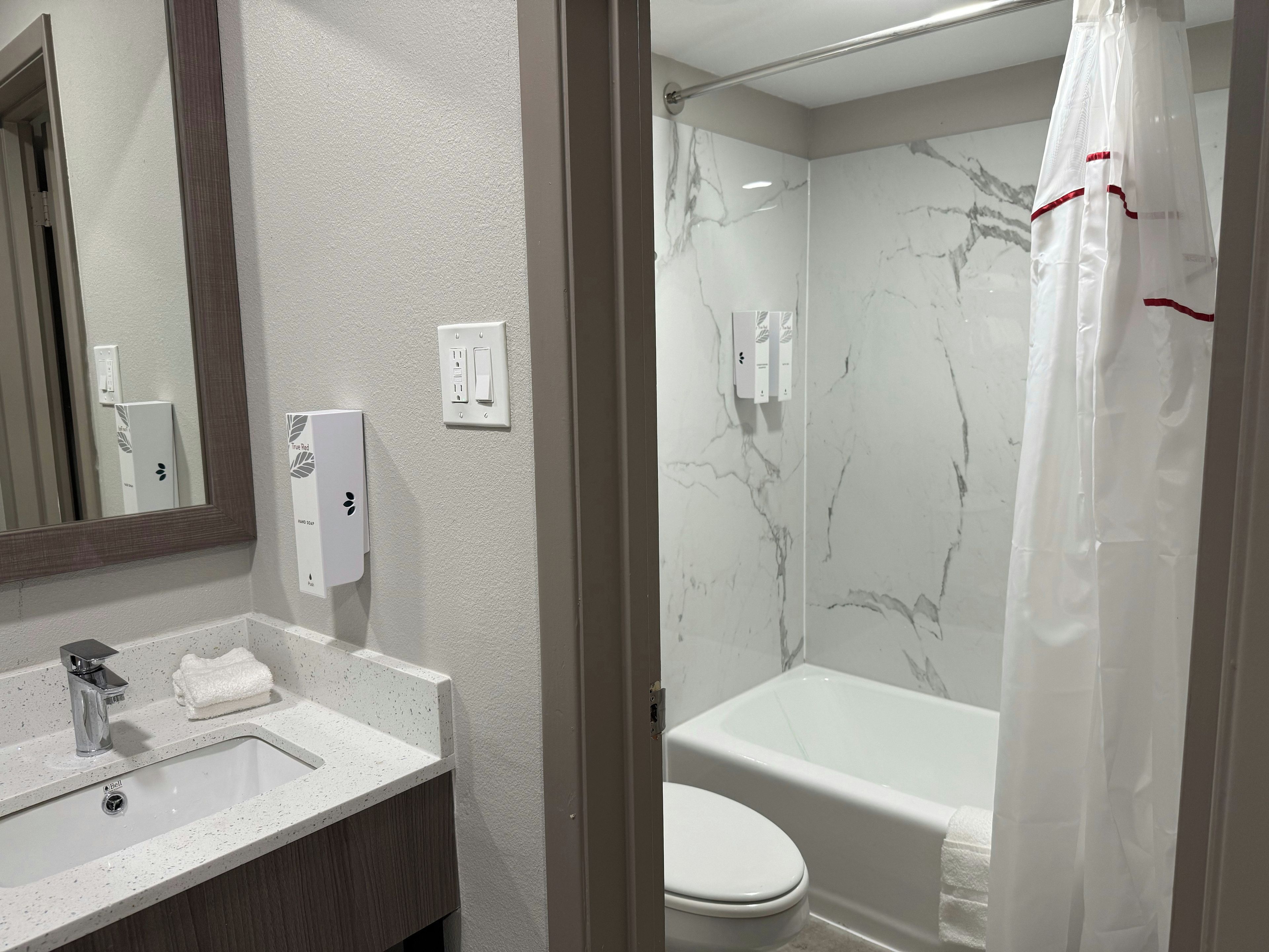 A bathroom with a marble wall, a bathtub, a toilet, a sink with a faucet, and a mirror.