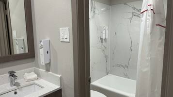 A bathroom with a marble wall, a bathtub, a toilet, a sink with a faucet, and a mirror.
